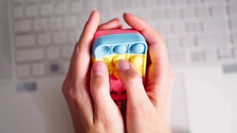 Finger drücken auf buntem Anti-Stress-Spielzeug rum; darunter liegt eine Tastatur