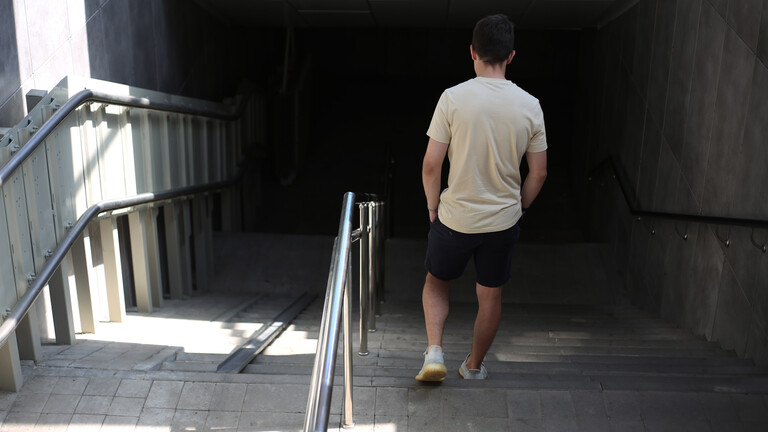 Ein junger Mann in T-Shirt und kurzen Hosen geht die Treppe von der Straße hinunter in die Unterführung zur U-Bahn.