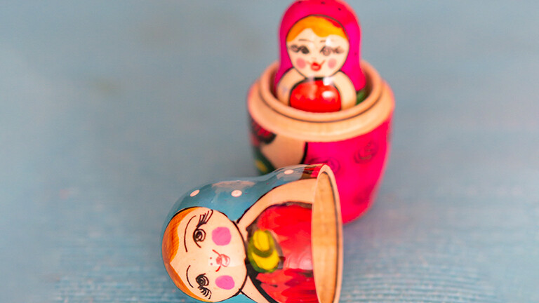 Eine Matrjoschka-Puppe aus Holz ist offen. Der obere Teil der Puppe liegt neben dem unteren. Darin ist eine kleinere Puppe zu sehen.
