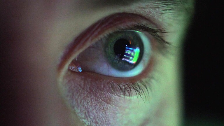Das Auge eines Mannes, der konzentriert auf einen Bildschirm schaut. Der Bildschirm spiegelt sich im Auge.