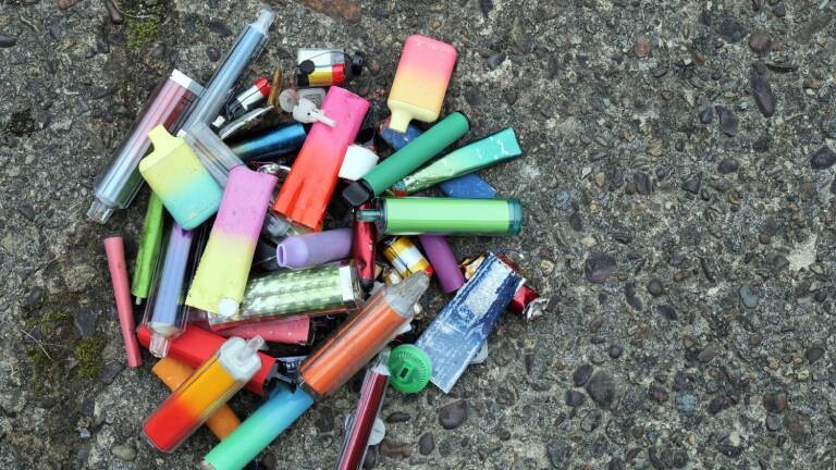 Eine Ansammlung leuchtender und bunter, weggeworfener Vapes wurde auf einem abgenutzten Betonboden zusammengelegt.