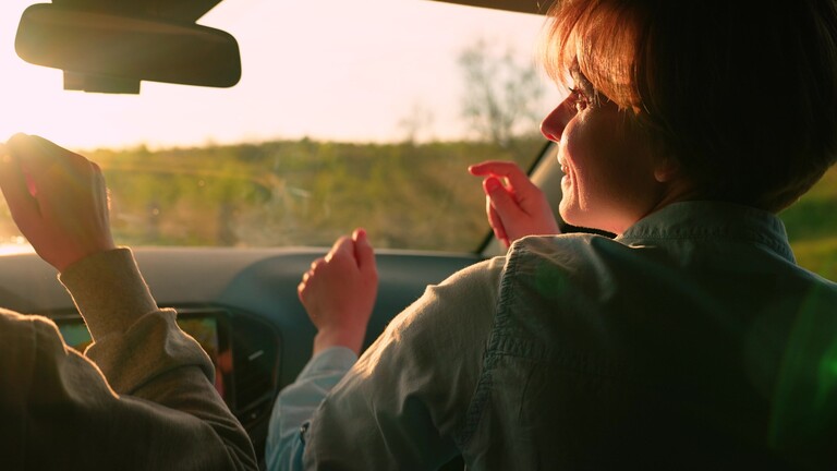 Junge Frauen fahren Auto, hören Musik und singen und tanzen im Sitzen während der Fahrt