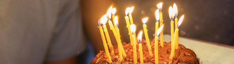 Ein junger Mensch lächelt, vor ihm ein Geburtstagskuchen mit brennenden Kerzen