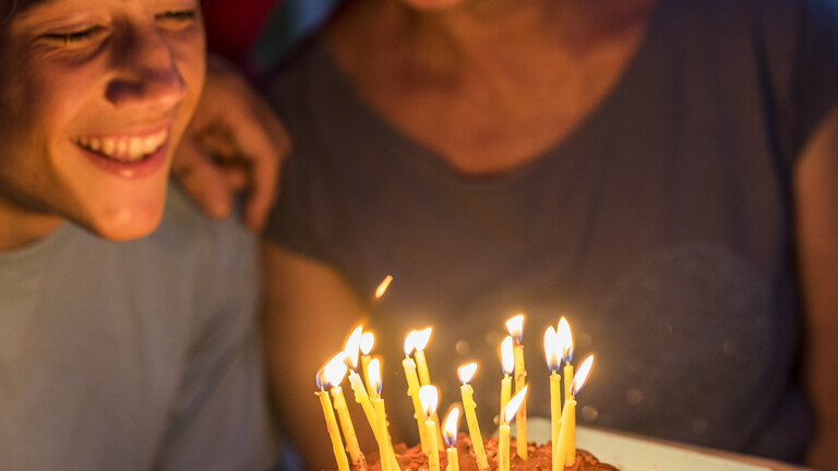 Ein junger Mensch lächelt, vor ihm ein Geburtstagskuchen mit brennenden Kerzen