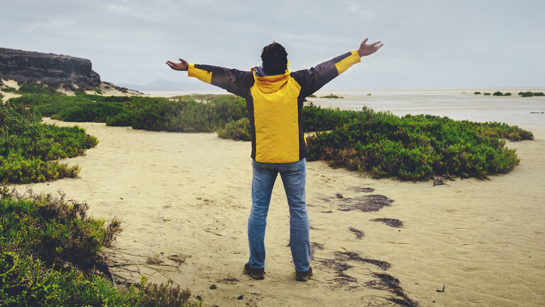 Ein Mann streckt an einem Strand anscheinend jubelnd die Arme aus.