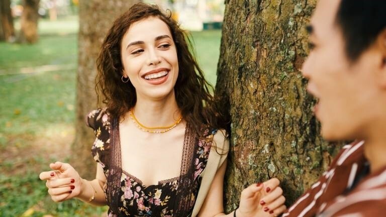 Eine Frau und ein Mann in einem Park an einen Baum gelehnt. Sieht nach einem Flirt aus.