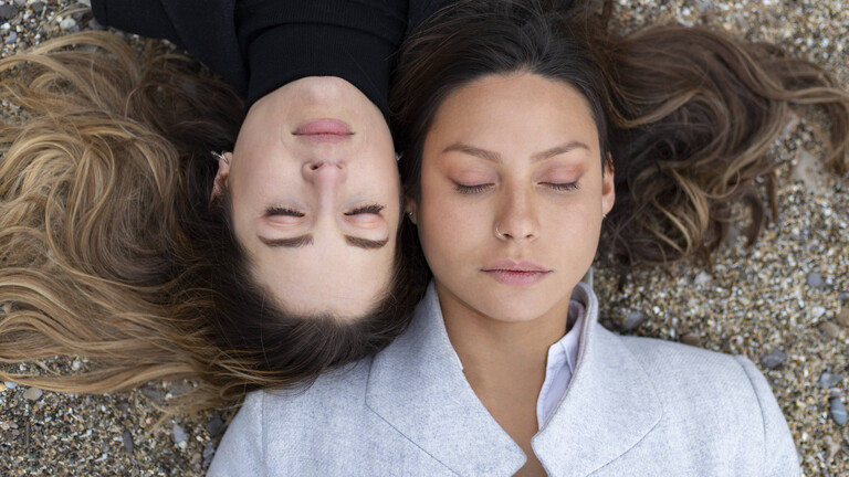 Zwei Frauen liegen versetzt zueinander auf dem Rücken und haben ihre Augen geschlossen. Ihre Köpfe liegen nebeneinander.