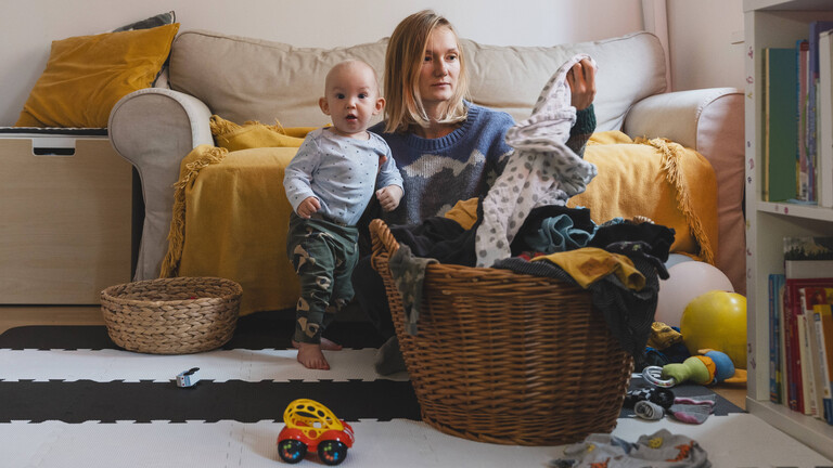 Foto einer jungen Frau, die mit ihrem Kind im Wohnzimmer auf em Boden sitzt und gewaschene Wäsche faltet