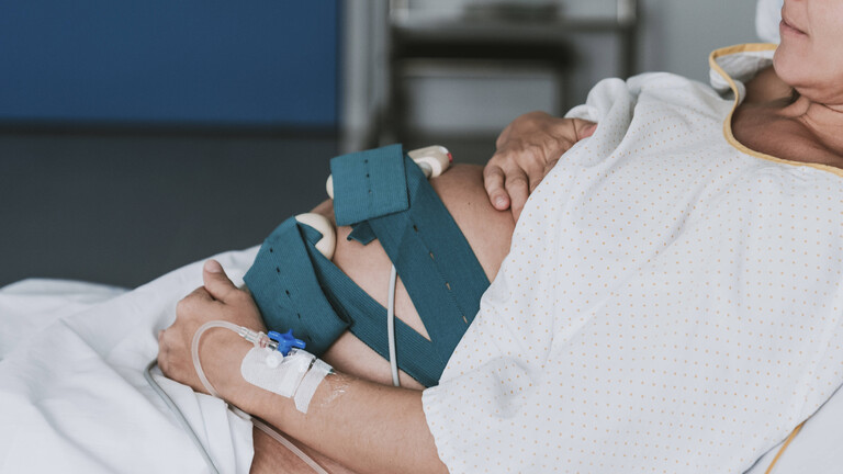 Schwangere Frau liegt mit den Händen auf dem Bauch im Krankenhaus.