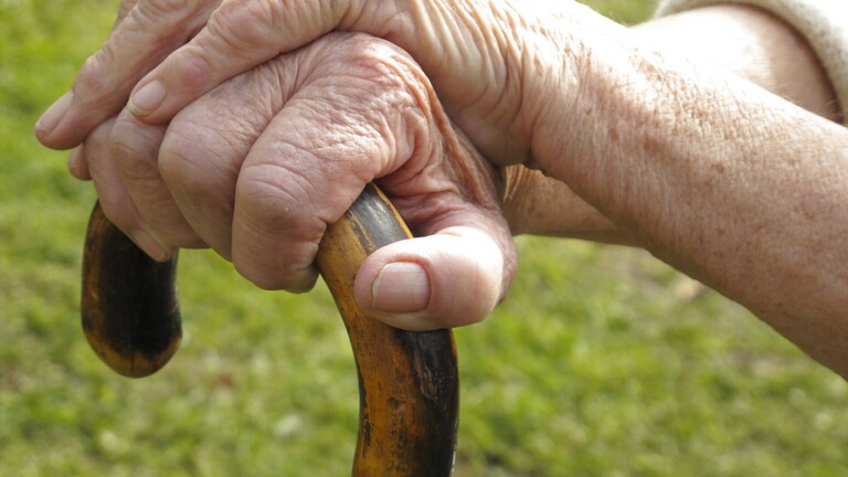 Hände einer alten Frau auf einem Stock