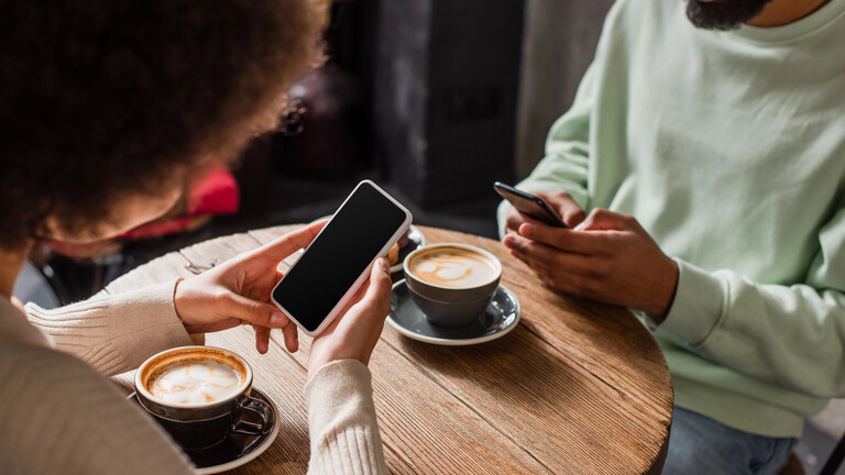 Ein Paar sitzt in einem Cafe. Beide blicken auf ihre Smartphones.
