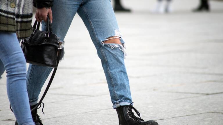 Zwei Frauen gehen mit einer Handtasche und zerrissenen Jeans über einen Platz