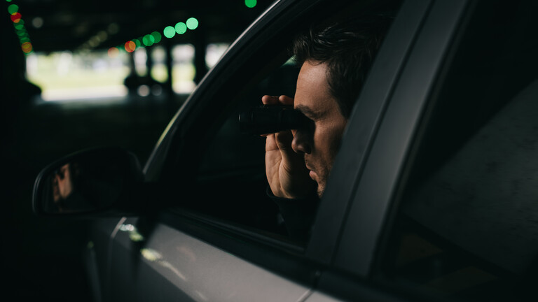 Ein Mann oberserviert aus einem Auto heraus mit einem Fernglas