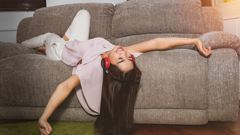 Eine Frau liegt auf dem Sofa, hört Musik und wirkt glücklich