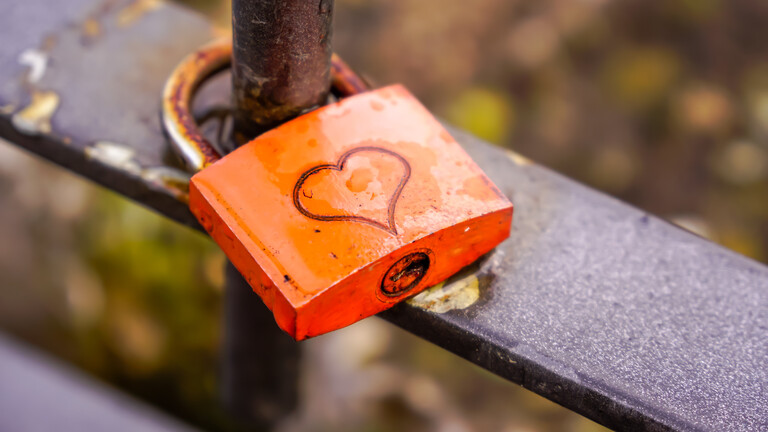 Ein leicht rostiges Liebesschloss an einem Zaun