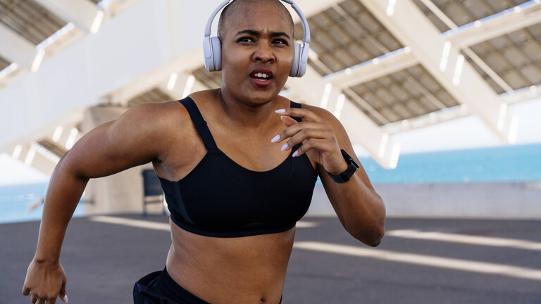 Eine Frau läuft auf einem Sportplatz. Sie trägt dabei Kopfhörer und schaut in die Ferne.
