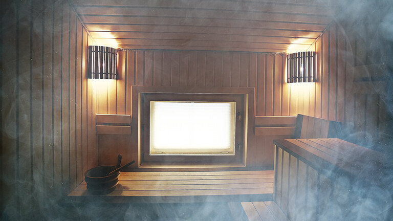Blick in eine leere Holzsauna, die von Dampf durchzogen ist