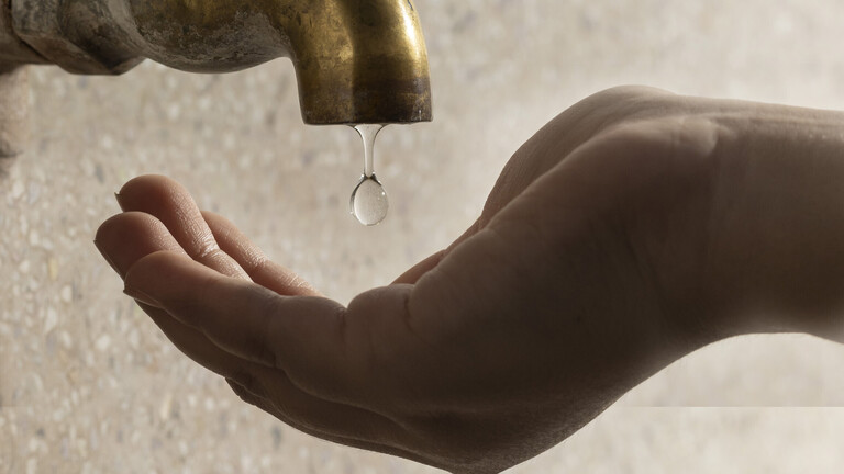 Nahaufnahme von Wasser, das von einem Messinghahn auf eine menschliche Hand tropft