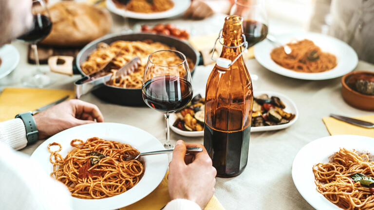 Gedeckter Tisch, andem Pasta serviert wird, und mehrere Personen sitzen