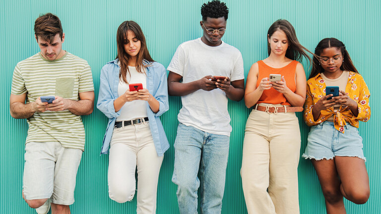 Einige Personen schauen auf ihre Smartphones während sie an einer Wand lehnen