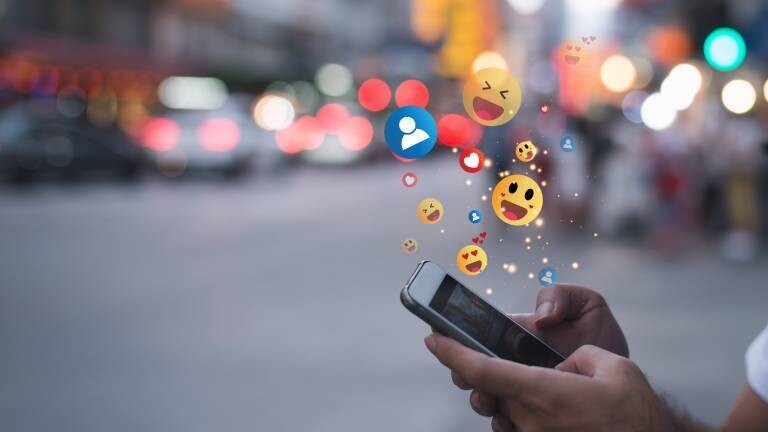Mensch tippt auf Smartphone, Emojis fliegen heraus