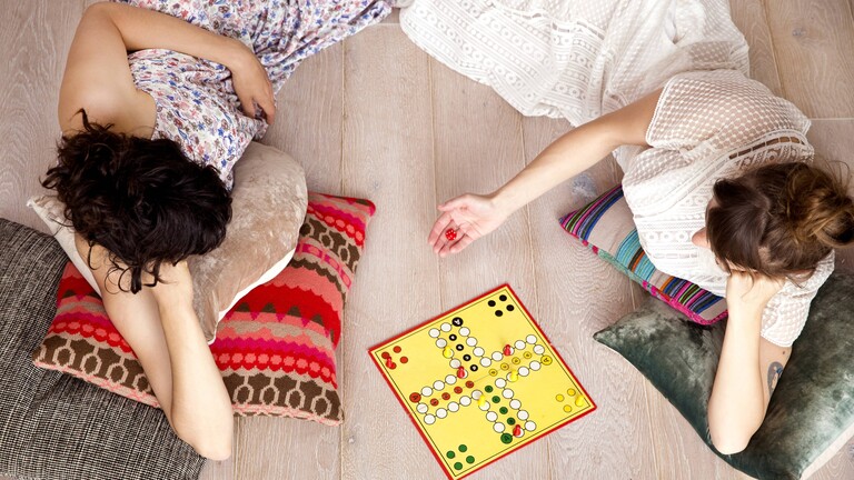 Foto von zwei jungen Frauen, die auf dem Fußboden Mensch ärgere dich nicht spielen