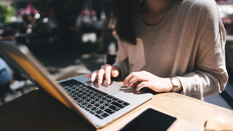 Eine Frau arbeitet im Cafe an ihrem Laptop und hat neben sich ein Smartphone liegen