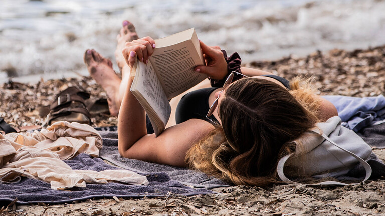 Eine Frau liegt am Strand und liest ein Buch.