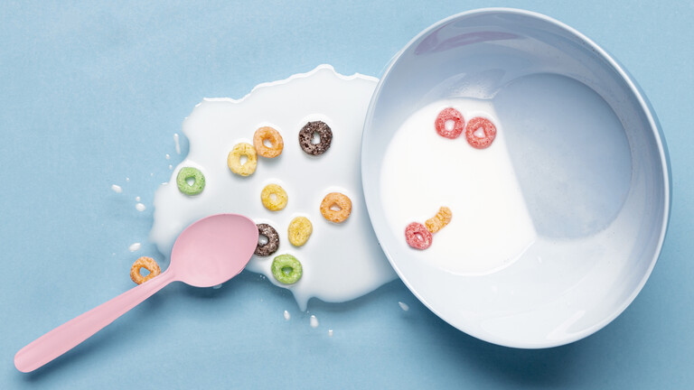 Verschüttete Milch neben einer Frühstücksschale mit bunten Cerealien