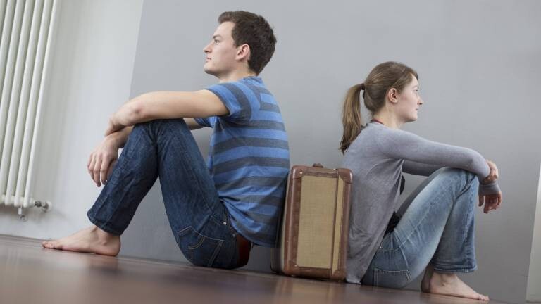 Mann und Frau sitzen mit dem Rücken zueinander auf dem Boden, zwischen ihnen steht ein Koffer