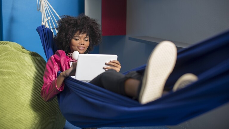 Eine Frau schaut etwas auf ihrem Tablet während sie in einer Hängematte liegt