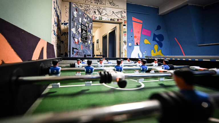 In einem Raum eines Jugendzentrums in Essen steht ein Kickertisch. Die Wände in dem Raum sind bunt angestrichen und teilweise mit Aufklebern beklebt.