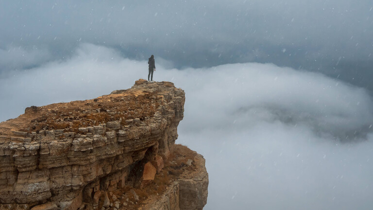Eine Person steht an einem Klippenrand auf einem Berg