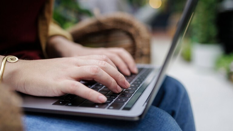 Eine Person sitzt draußen und hat einen Laptop auf dem Schirm. Sie tippt.