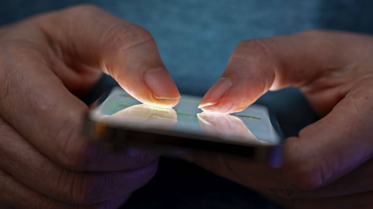 Eine Person hält in seinen Händen ein Handy und tippt darauf mit den beiden Daumen.