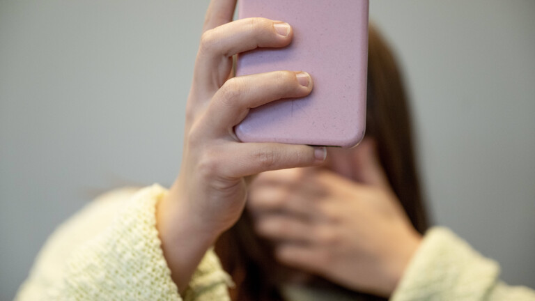 Eine Frau reagiert, sie hat eine schockierte Reaktion auf etwas, das sie auf ihrem Handy sieht