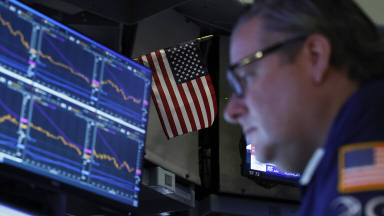 Ein Börsenhändler vor einem Bildschirm mit Aktienkursen, dahinter eine USA-Flagge