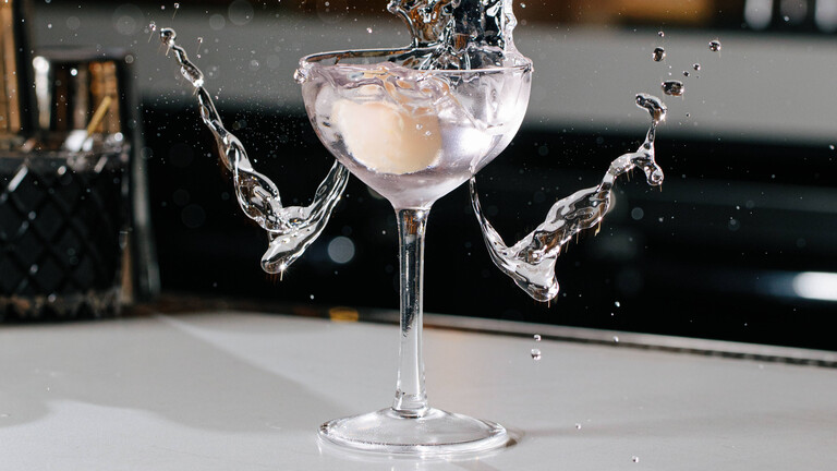 Aus einem gefüllten Cocktail-Glas schwappt an den Seiten das Getränk raus.