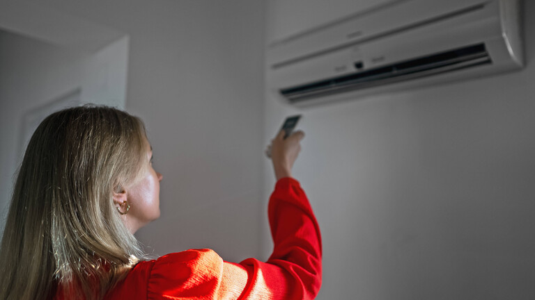 Eine Frau richtet eine Fernbedienung auf eine festeingebaute Klimaanlage, die an der Wand hängt.