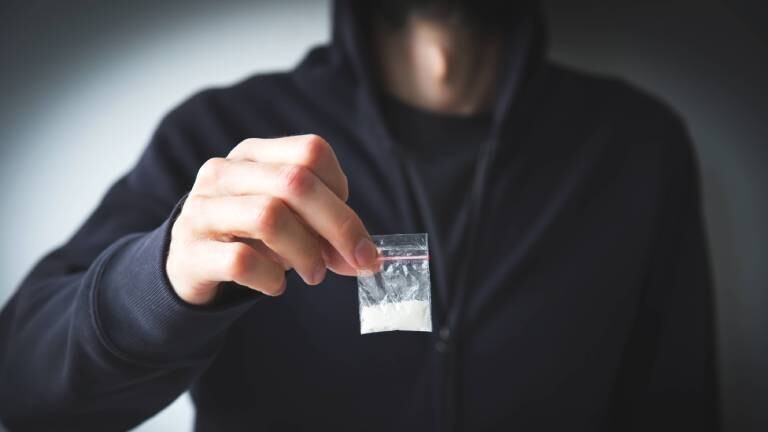 Person in Sweatshirt und Kapuzenpulli hält kleine Tüte mit weißer Substanz