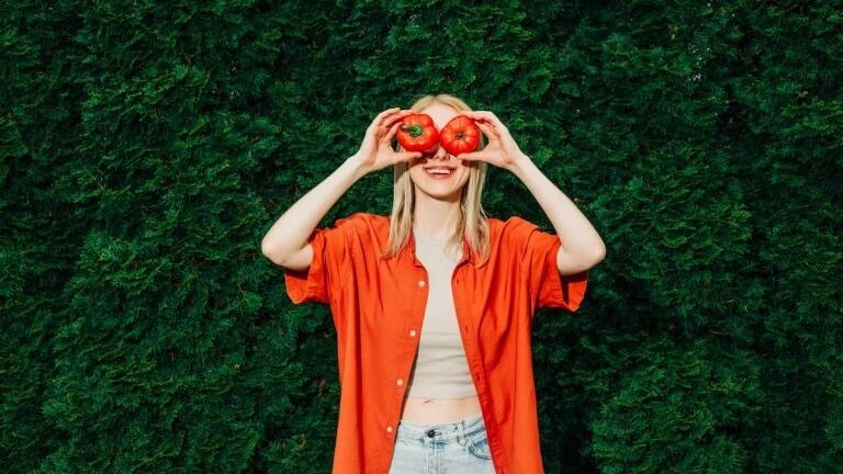 Eine Frau hält sich eine Paprika und eine Tomate vor die Augen