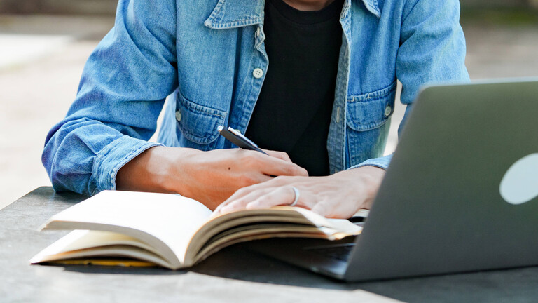 Student beim E-Learning mit einem Laptop auf einer Bank auf dem Campus.