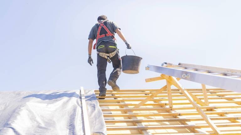 Dachdecker geht mit Eimer in der Hand über ein Dach