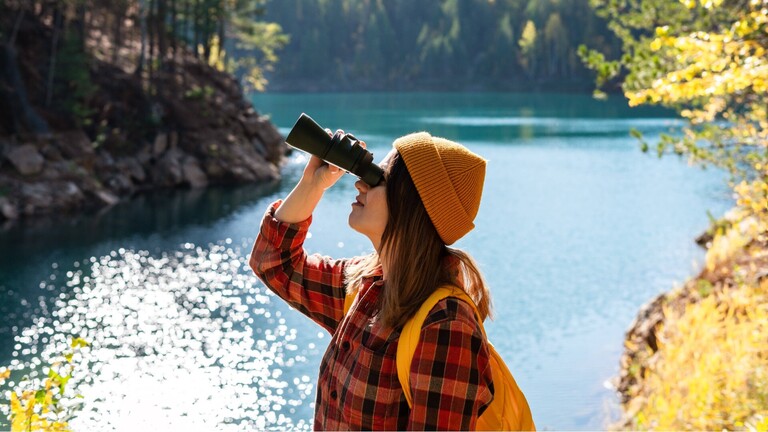 Frau mit Wollmütze, Karohemd und Fernglas in der Natur.
