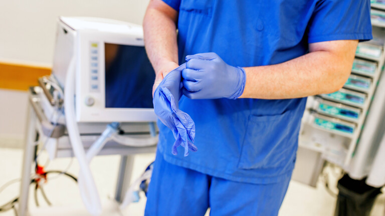 Ein Arzt in blauer Kleidung zieht sich blaue OP-Handschuhe an.