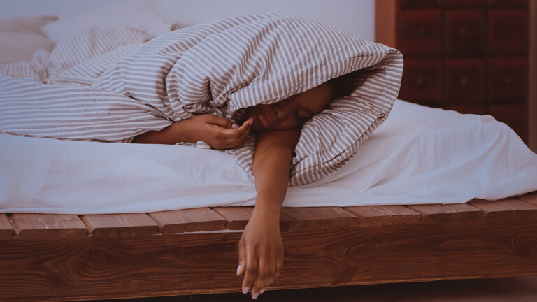 Eine Frau schläft in eine Decke gehüllt auf dem Bett in ihrem Schlafzimmer