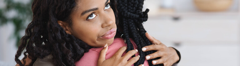 Junge Frau rollt mit den Augen während sie eine Freundin umarmt.