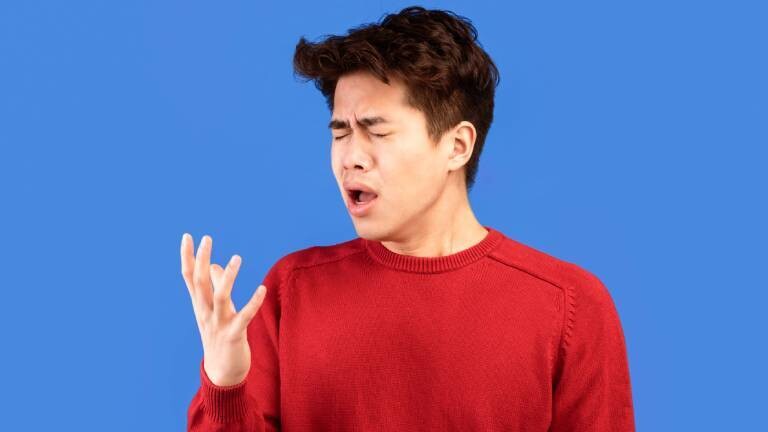 Mann in rotem Pullover vor blauem Hintergrund verzieht das Gesicht, als ob er niesen oder husten müsste