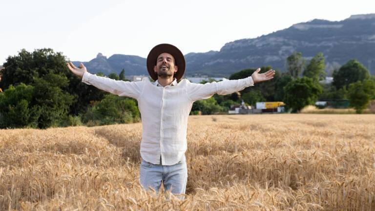 Ein Mann steht mit ausgebreiteten Armen in einem Getreidefeld