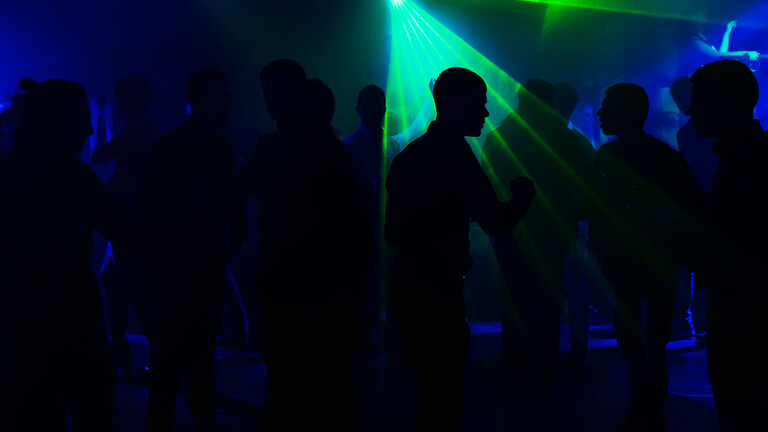 Eine Gruppe Menschen tanzt in einem Club. Von den Menschen sind nur die Silhouetten erkennbar, weil es relativ dunkel ist.